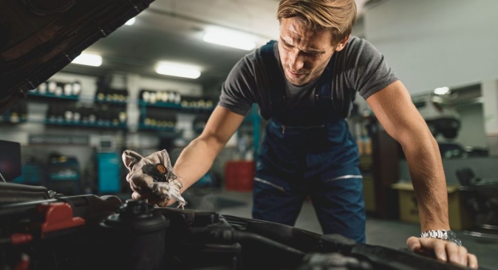 Jeune mécanicien vérifiant le circuit de refroidissement du radiateur en atelier auto