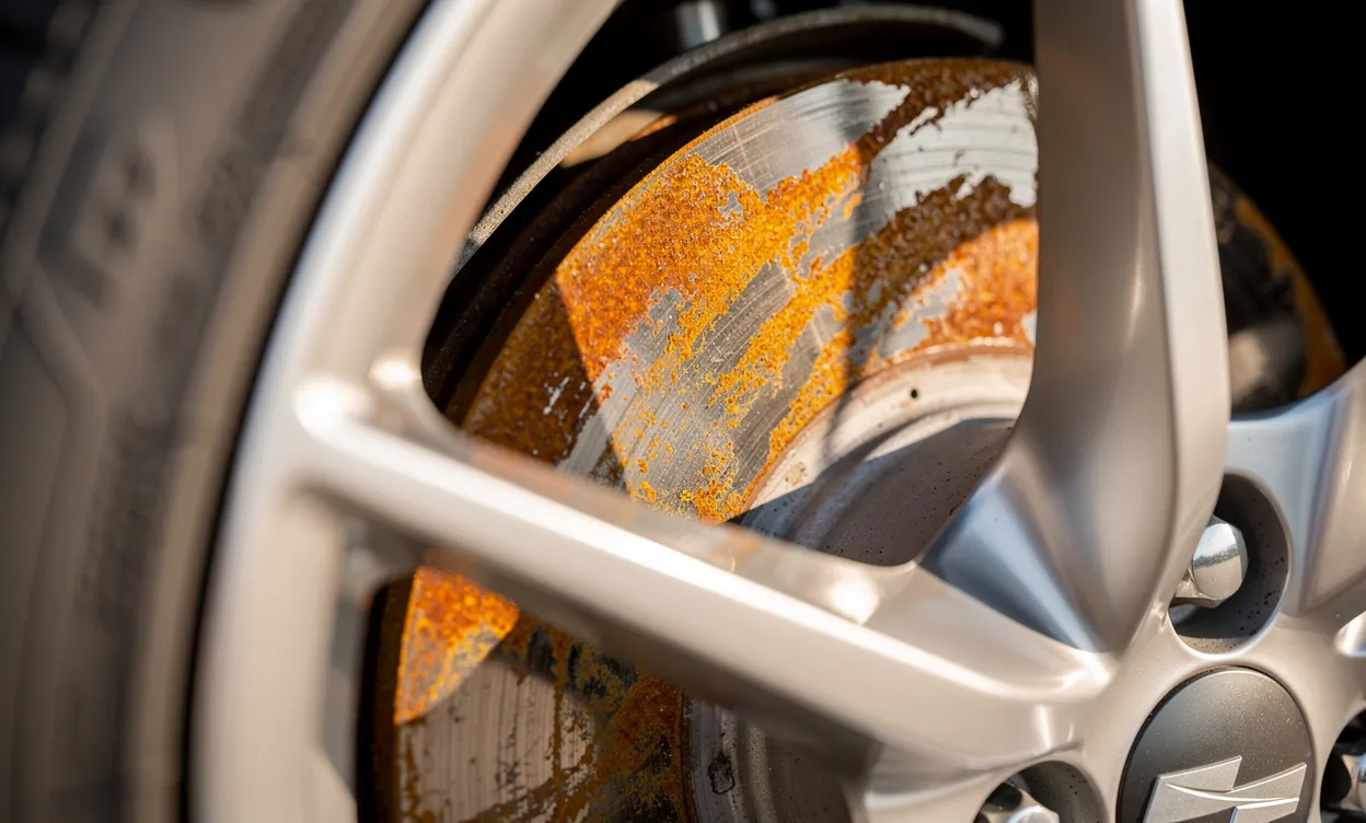 Gros plan sur une roue de voiture montrant un disque de frein marqué par des taches de rouille orange sous une lumière douce.