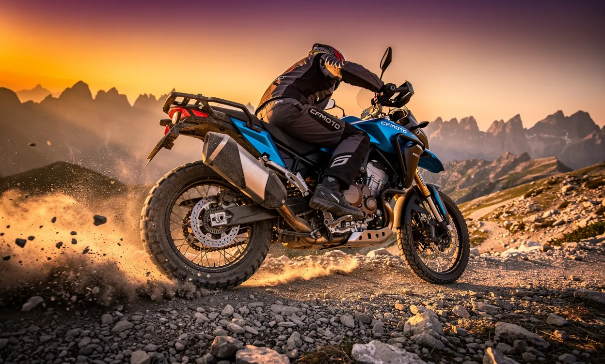 Une moto CFMoto 1000 MT-X bleu et noire soulève de la poussière en roulant sur un sentier de montagne au coucher du soleil.
