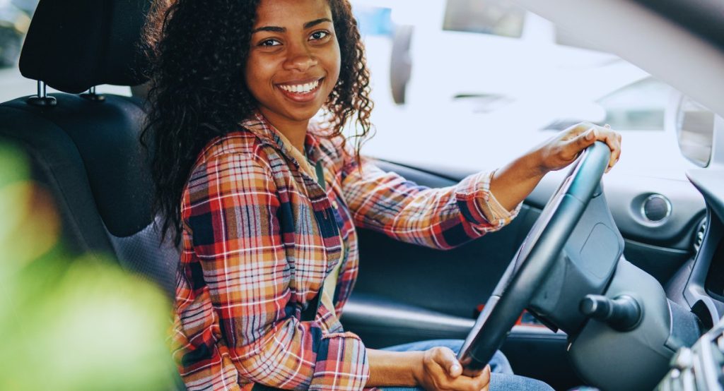 Jeune femme souriante au volant d'une voiture, les mains sur le volant