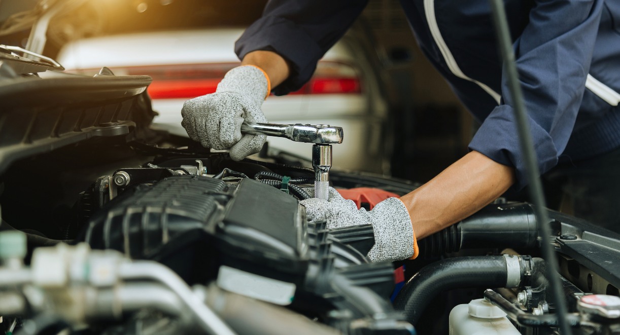 Mécanicien avec clé à cliquet intervenant sous le capot d'une voiture au garage