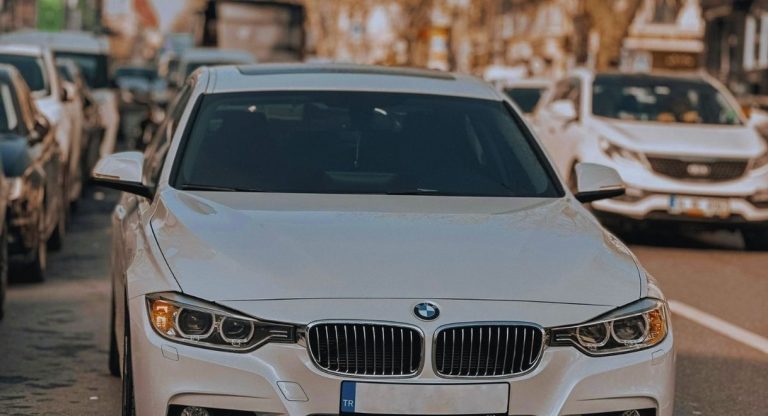 Berline BMW blanche vue de face dans une rue en circulation, calandre et phares en premier plan