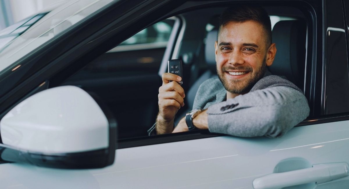 Homme souriant a la fenetre d'une voiture blanche en tenant une cle de contact