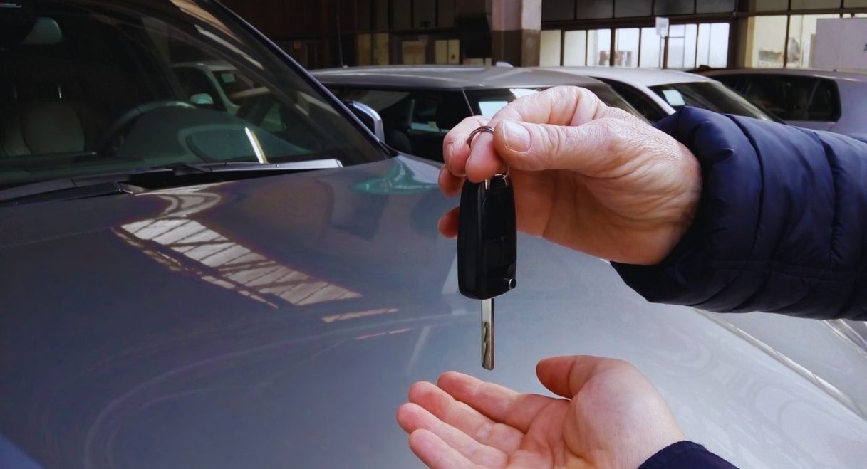 Remise d'une clé de voiture entre deux mains devant un capot gris dans un garage