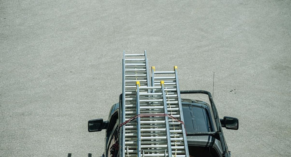 Vue de dessus de deux échelles en aluminium fixées par une sangle sur le toit d'un véhicule utilitaire
