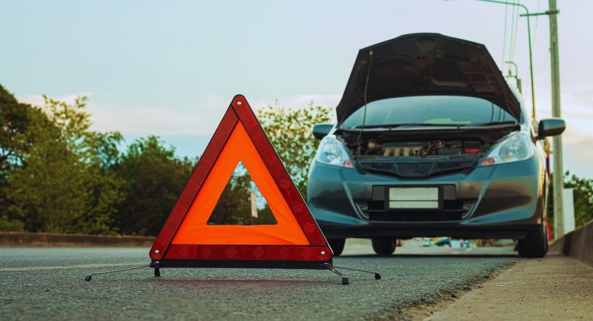 Triangle de signalisation rouge posé sur la route devant une voiture grise arrêtée, capot ouvert
